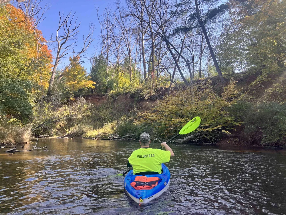 Kayaker paddling the Lower Waupaca River beneath high banks and autumn trees